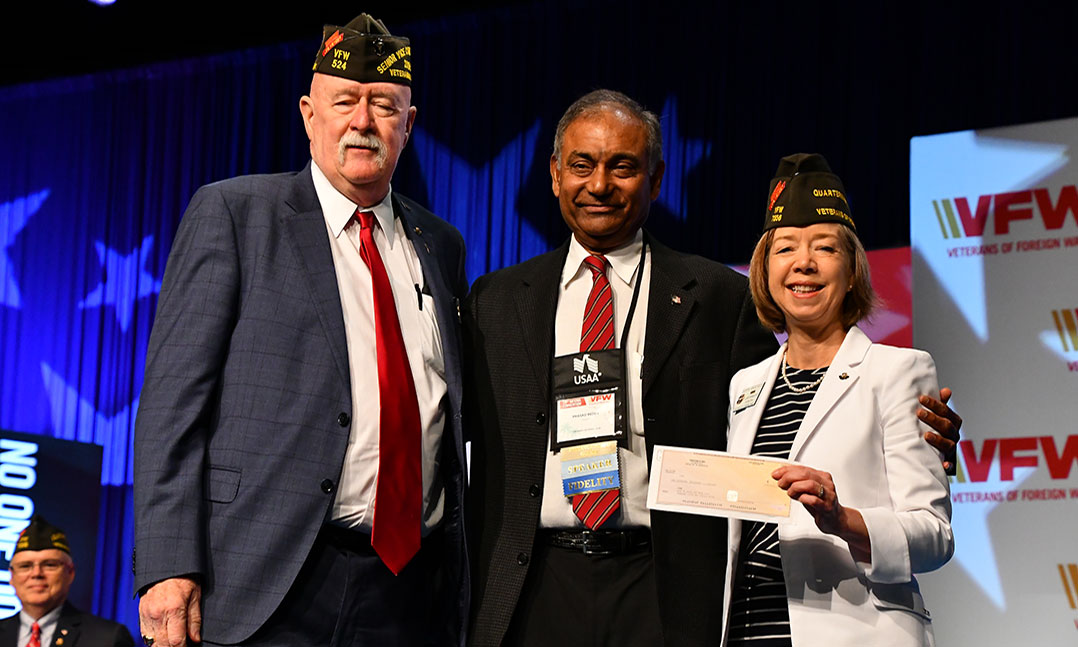 VFW National Commander Doc Schmitz, left, and VFW Quartermaster General Debra Anderson, right, accept a $100,000 check from Prasad Reddy with Twisted X in support of VFW youth programs