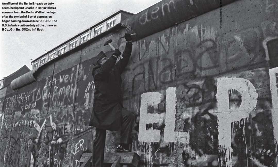 An Berlin Brigade officer near Checkpoint Charlie in Berlin takes a souvenir from the Berlin Wall