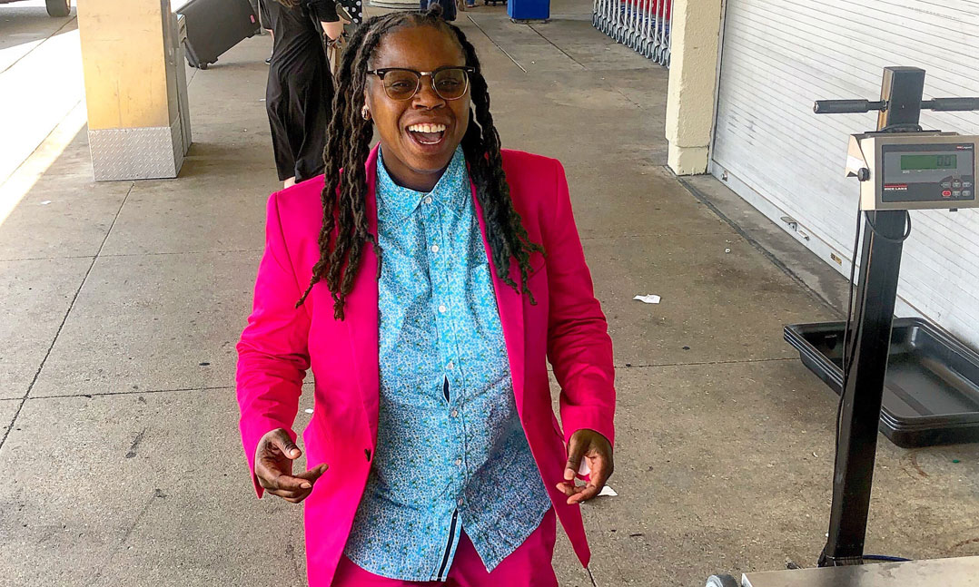 A smiling woman veteran in a pink suit walks down a sidewalk