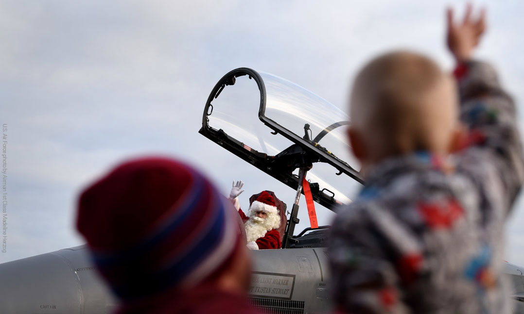 Child waving to Santa who is sitting in a fighter yet