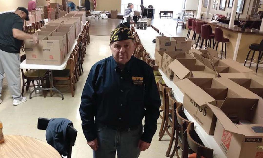 Veteran stands before boxes ready to collect items for veterans in need