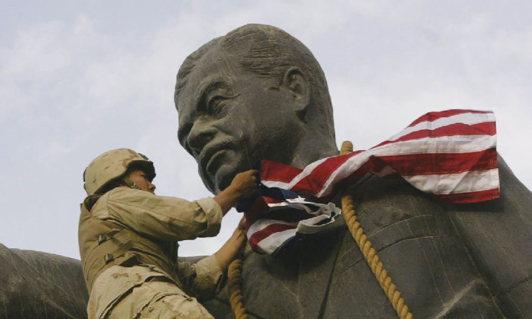 Marine Cpl. Edward Chin of 3rd Bn., 4th Marines, covers the face of a statue of Saddam Hussein with a U.S. flag