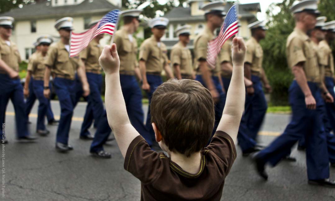 small child waiving flags in front of Marines on parade